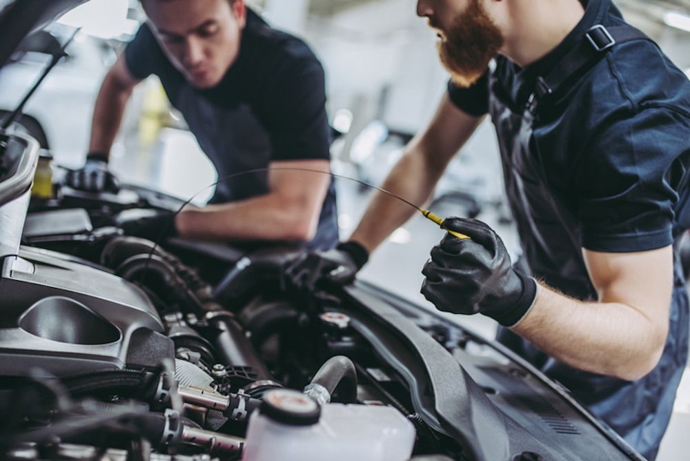 Two technicians checking the oil in a vehicle