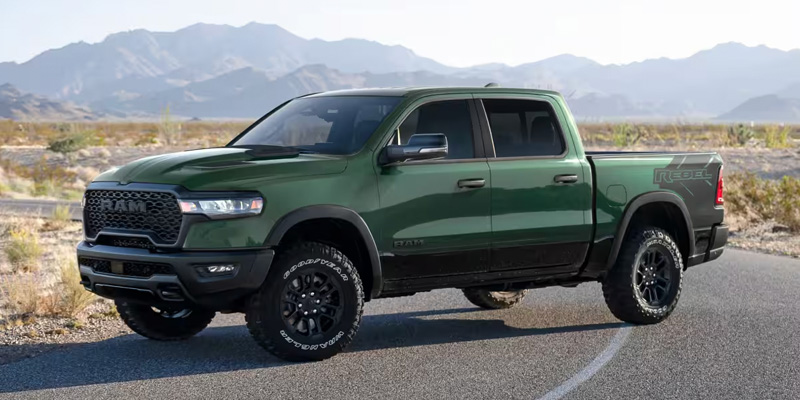 The image showcases a rugged green RAM 1500 Rebel, emphasizing its bold and adventurous design, perfect for off-road excursions, with a stunning mountainous backdrop.
