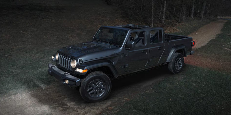 Dark grey Jeep Gladiator parked on a wooded trail at night.
