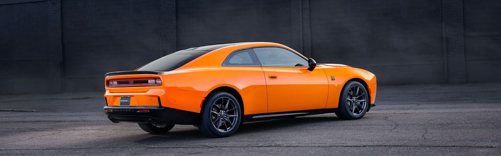 Rear view of an orange Dodge Charger parked in front of a dark brick wall.