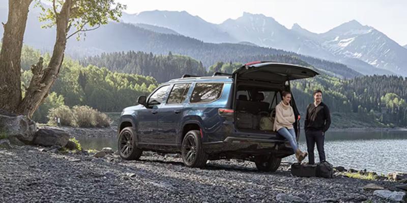 Blue SUV parked by a mountain lake with two people standing near the open trunk.