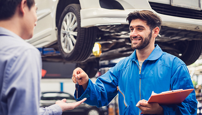Smiling auto mechanic handing car keys to a customer in an auto repair shop.